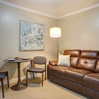 A cozy living room setup featuring a brown sofa, a small table with two chairs, and an abstract artwork on the wall.