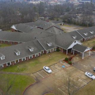 Aerial view of a large building with a parking lot and surrounding trees.