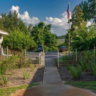 A sunny garden pathway leading to a flag with lush greenery and a clear sky.
