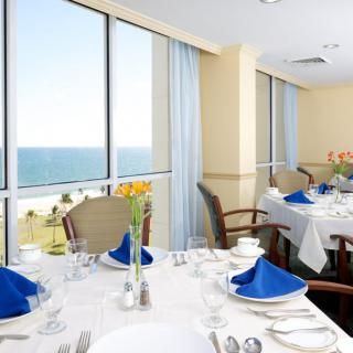 An elegantly set dining table with blue napkins, overlooking a scenic ocean view through large windows.