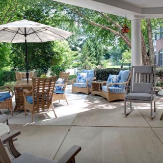 A cozy patio with comfortable seating and a dining area under a sun umbrella, surrounded by lush greenery.