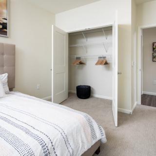 A minimalist bedroom with an open closet and a neatly made bed.