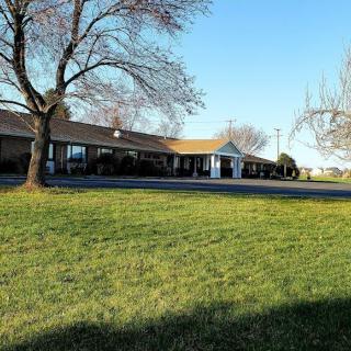 A scenic view of a single-story building surrounded by trees and grass under a clear blue sky.