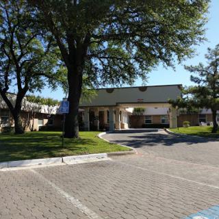 A sunny day showcasing a building surrounded by trees and a neatly paved parking area.