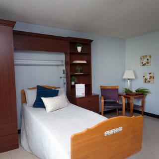 A simple hospital room with a single bed, wooden furniture, and minimal decor.