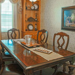 A traditional dining room with a wooden table and chairs, adorned with elegant decor and a framed painting on the wall.