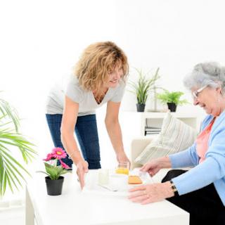 A caregiver assists an elderly woman with a meal in a bright and welcoming environment.