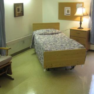 A simple hospital room with a single bed, nightstand, and lamp.