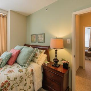 A cozy bedroom with floral bedding, colorful pillows, and a warm lamp on the nightstand.