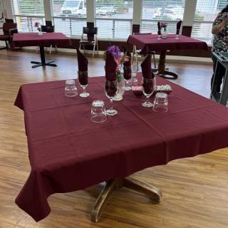 Elegantly set dining tables with maroon tablecloths and folded napkins in a restaurant.