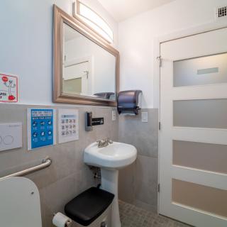 An accessible bathroom featuring a sink, mirror, handrail, and paper towel dispenser.