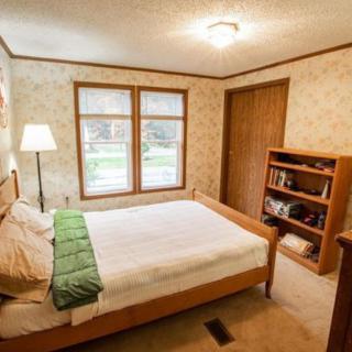 A cozy bedroom with a wooden bed, decorated with a green throw, and a large window allowing natural light.