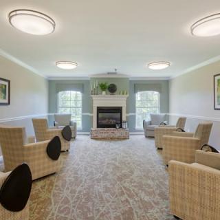 A cozy living room with a fireplace, surrounded by comfortable chairs and large windows.