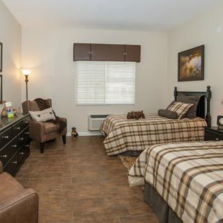 A cozy bedroom featuring twin beds with plaid bedding, a comfortable armchair, and warm lighting.