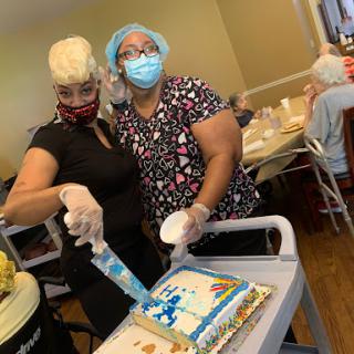 Two women preparing a cake for a celebration while wearing masks.