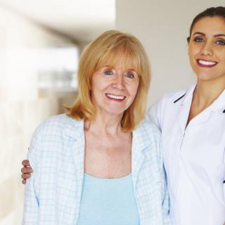 An elderly woman stands next to a smiling nurse in a healthcare setting.
