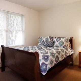 A cozy bedroom with a wooden bed frame, patterned bedding, and a bedside lamp.