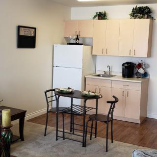 A compact kitchen and dining area in an apartment, featuring a small table with chairs, a refrigerator, and overhead cabinets.