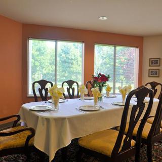 A well-lit dining room with a table set for a meal, featuring elegant chairs and floral centerpiece.