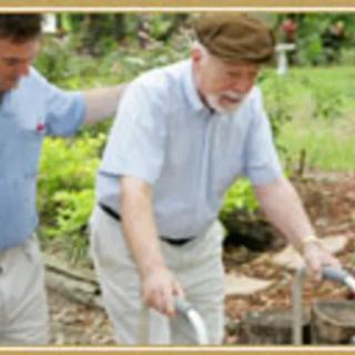 A caregiver assists an elderly man using a walker in a garden setting.