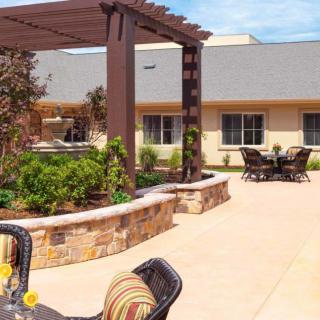 A beautiful outdoor patio area with seating and a pergola, surrounded by a landscaped garden under a clear blue sky.