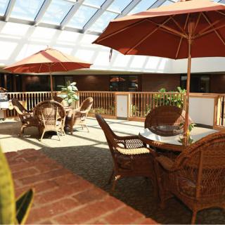 A bright indoor seating area with wicker furniture and umbrellas under a skylight.