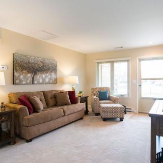A cozy living room with a sofa, armchair, and natural lighting from the windows.