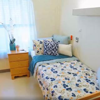 A cozy and neatly arranged bedroom featuring floral bedding, decorative pillows, and natural light.