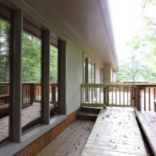 A wooden deck with railing and large windows overlooking a natural setting.