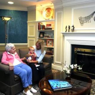 A cozy living room scene with a family gathering near the fireplace, featuring an elderly person and a baby.