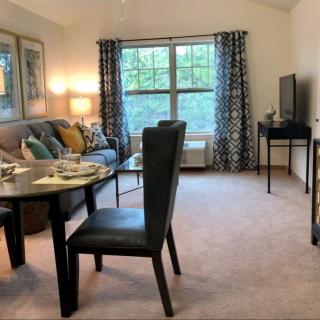 A cozy living room with a dining area, featuring a sofa, dining table set, and a television beside a large window.