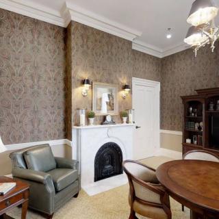 A cozy living room with a classic fireplace, elegant wallpaper, and comfortable seating.