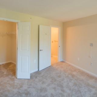 An empty bedroom with carpeted flooring, featuring a closet and open doors.