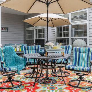 A cozy patio setup with striped cushioned chairs and a colorful rug under a large umbrella.