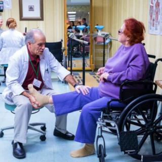 A doctor examines a patient's leg in a wheelchair at a clinic.