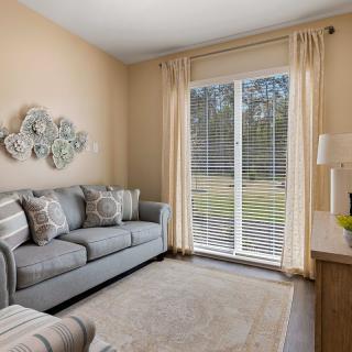 A cozy living room featuring a gray sofa, decorative pillows, and a large window with blinds and curtains.