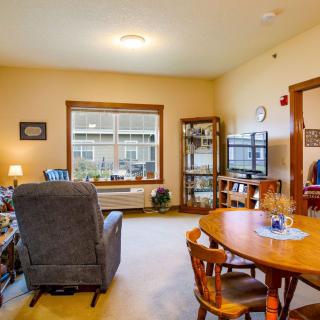 A cozy living room with a dining area, featuring a comfortable chair, bookshelves, and a TV.