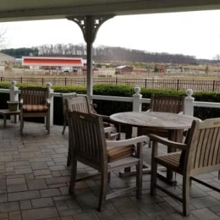 A cozy outdoor patio with wooden furniture overlooking a countryside farm.