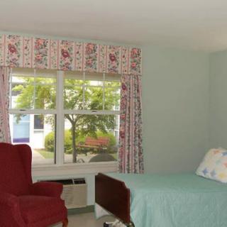 A cozy bedroom with a red chair, a bed, and floral curtains framing the window.