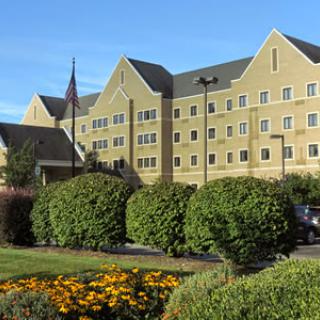 A view of a hotel surrounded by well-kept bushes and flowers under a clear blue sky.