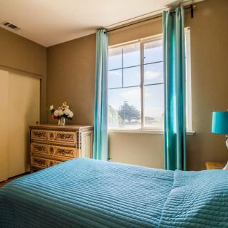 A cozy bedroom with blue curtains and bedding, featuring a wooden dresser and a bedside lamp.