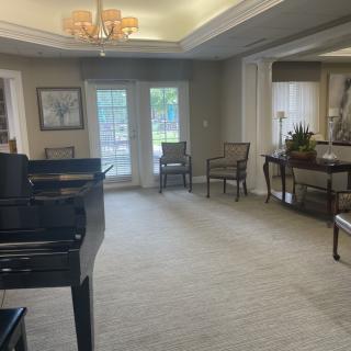 A spacious living room with a grand piano, elegant furniture, and large windows.