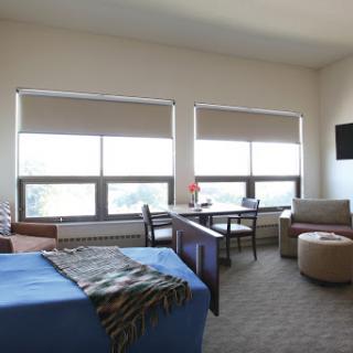A well-lit and modern room featuring large windows, comfortable seating, and a neatly made bed.