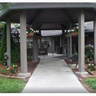 A covered walkway leads through a garden area with hanging flower baskets and landscaping.