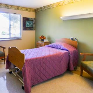 A cozy hospital room featuring a single bed with purple bedding, a small nightstand, and a comfortable chair.