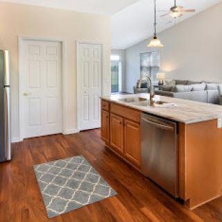 A modern kitchen featuring wooden cabinets, stainless steel appliances, and a cozy gray rug.