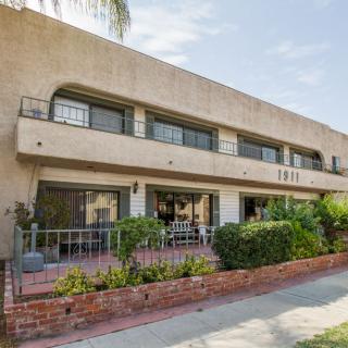 A modern two-story apartment building with balconies and lush landscaping on a sunny day.