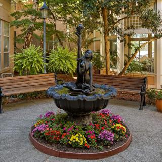 A small fountain with a statue in the center of an indoor courtyard, surrounded by colorful flowers and benches.