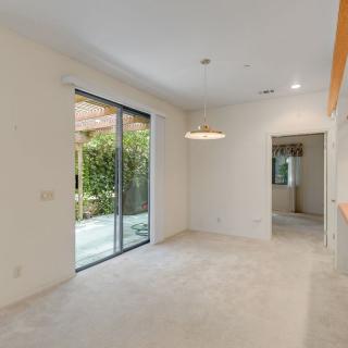 An empty living room with a carpeted floor and sliding glass doors opening to an outdoor area, illuminated by natural light.