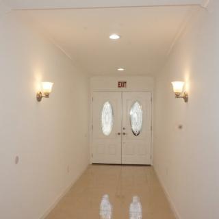 A brightly lit hallway with sconces and double doors at the end.